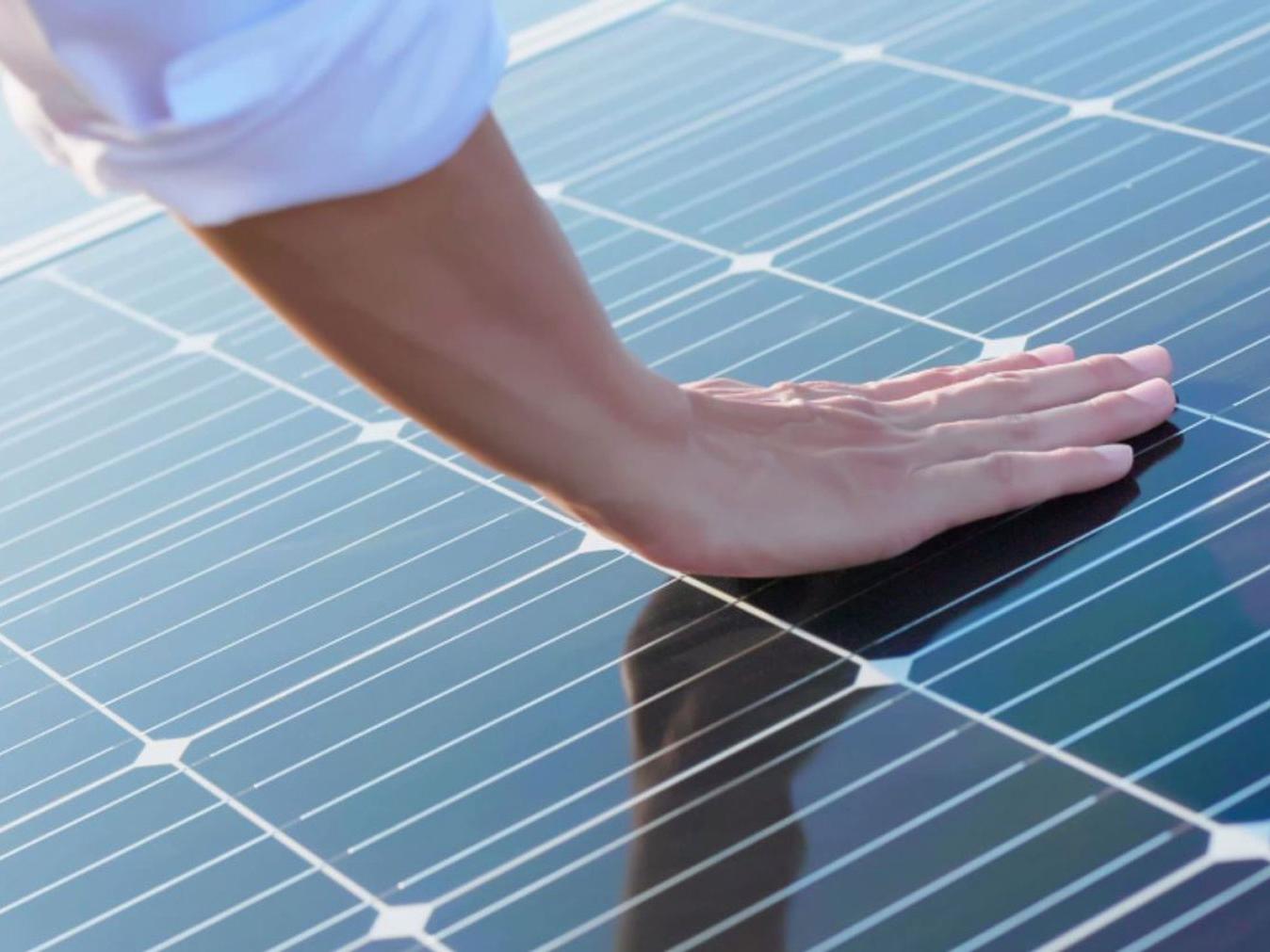 Een hand die fotovoltaïsche modules aanraakt. 