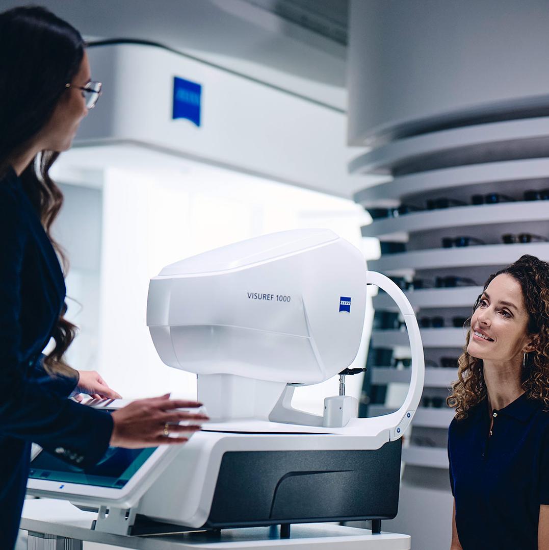 Une femme est assise devant le ZEISS VISUREF 1000, le regard tourné vers une opticienne.