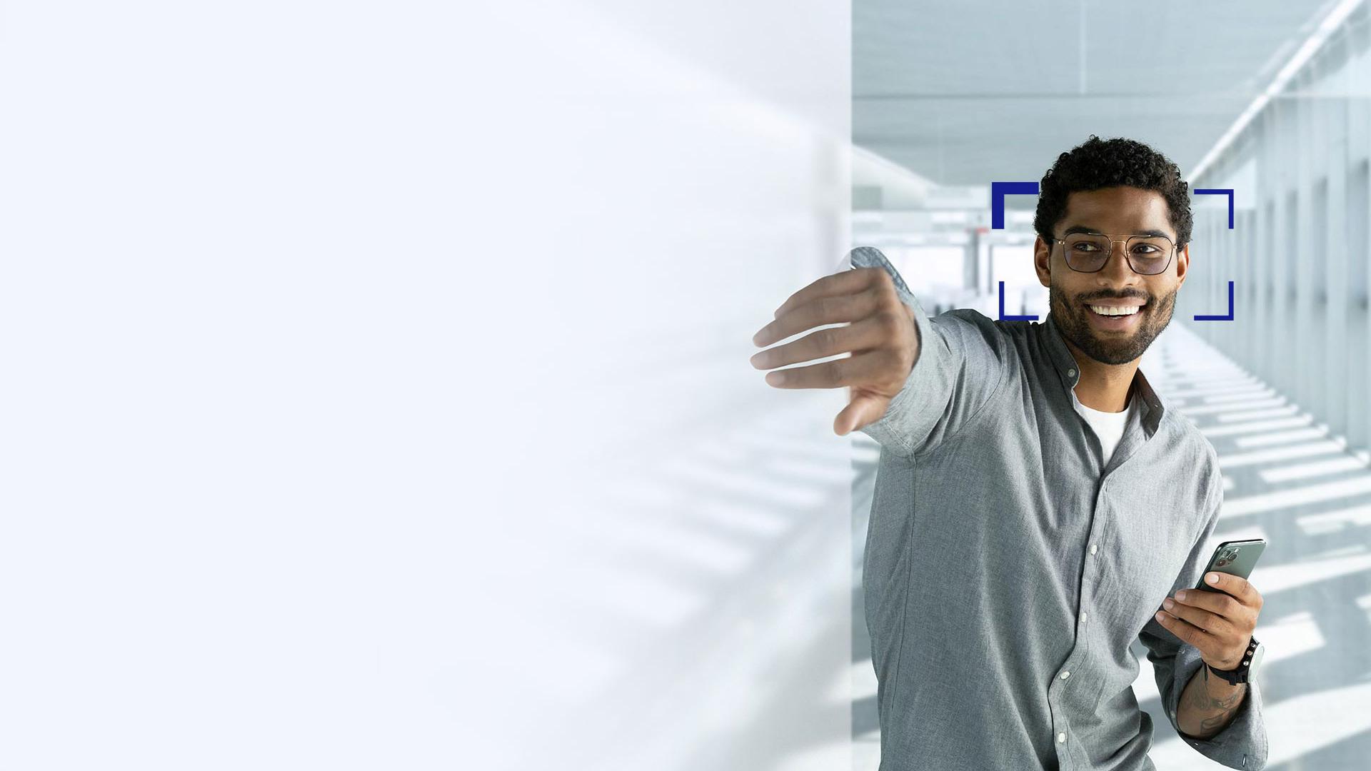 Un jeune homme aux cheveux noirs porte des verres ZEISS SmartLife et sourit en passant la main à travers un écran.