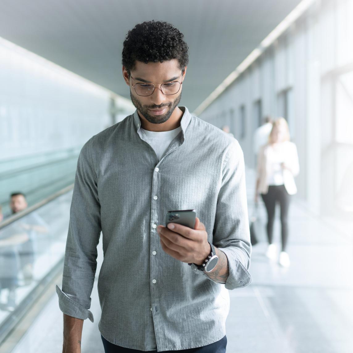 Jonge man die ZEISS SmartLife brillenglazen draagt en naar zijn telefoon kijkt terwijl hij loopt.