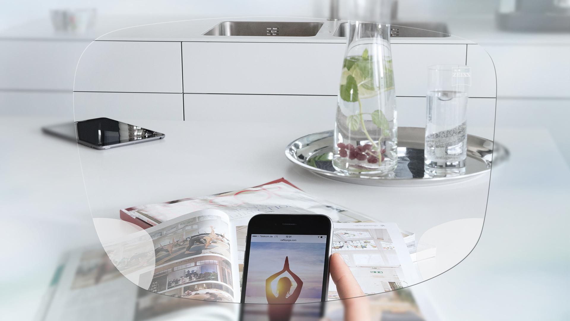 Zicht door een ZEISS EnergizeMe enkelvoudig brillenglas van een smartphonescherm en goed georganiseerde keukentafel 