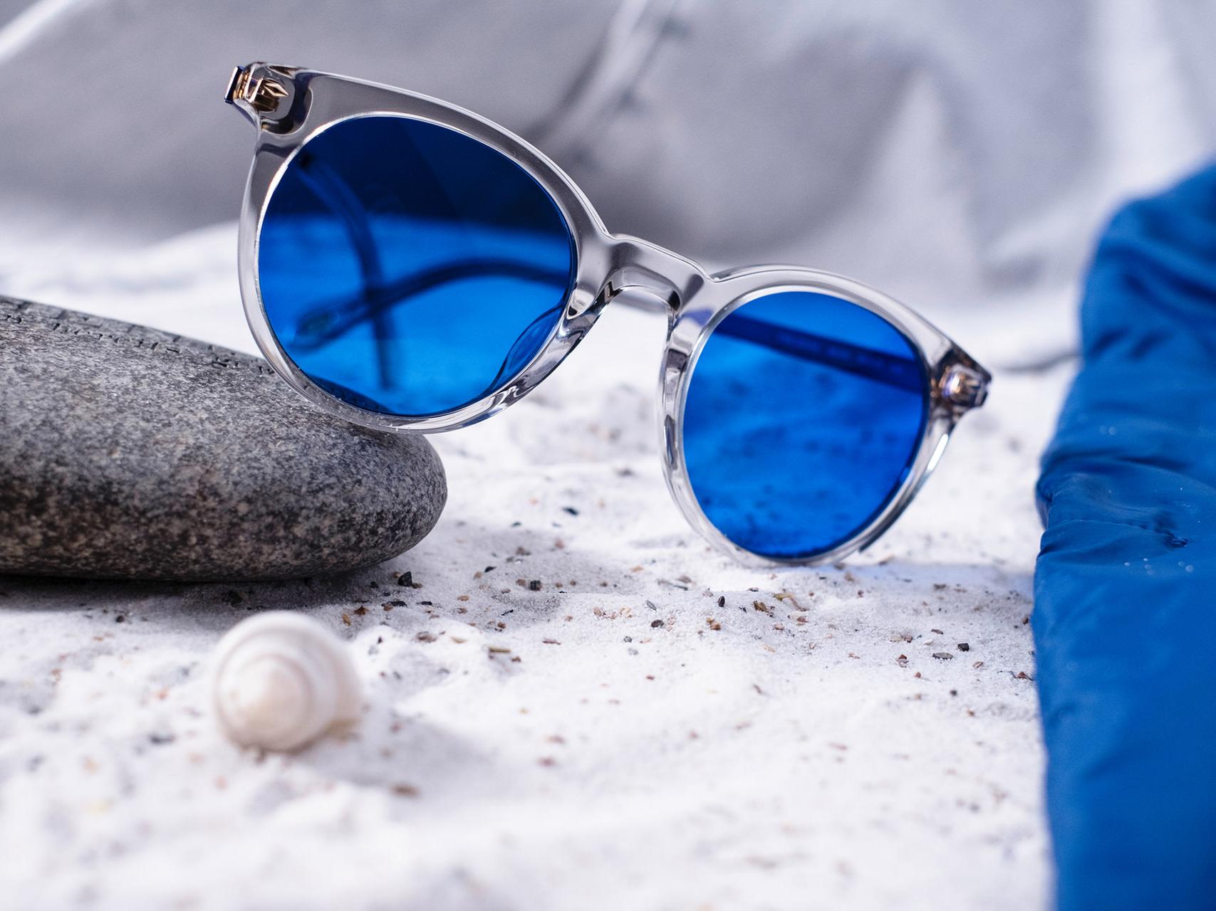 Foto van een zonnebril met blauwe tint, half op een steen gelegd