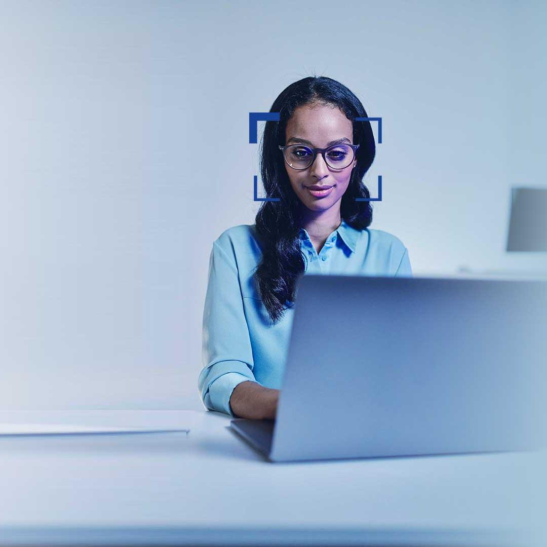 Vrouw met zwart haar en een bril kijkt met een lach op haar gezicht naar een laptop