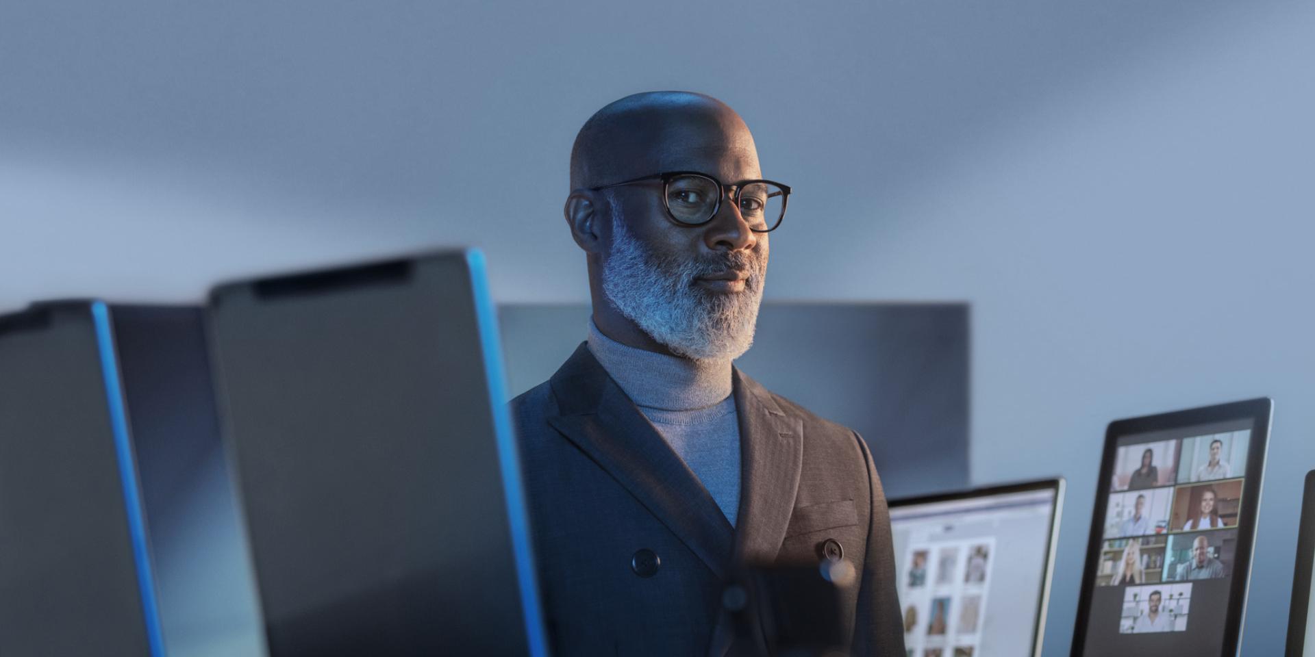 Lachende man omringd door digitale apparaten die een bril draagt met ZEISS BlueGuard voor bescherming tegen blauw licht.
