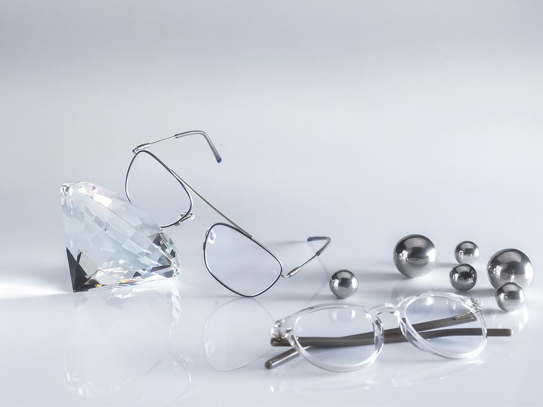 Twee brillen met ZEISS brillenglazen met de hardste en meest hygiënische ZEISS coating ooit - DuraVision® AntiVirus Platinum. Eén bril leunt tegen een kristal, de andere ligt plat op de grond naast zilver. Beide hebben heldere brillenglazen zonder blauwachtige reflectie. 
