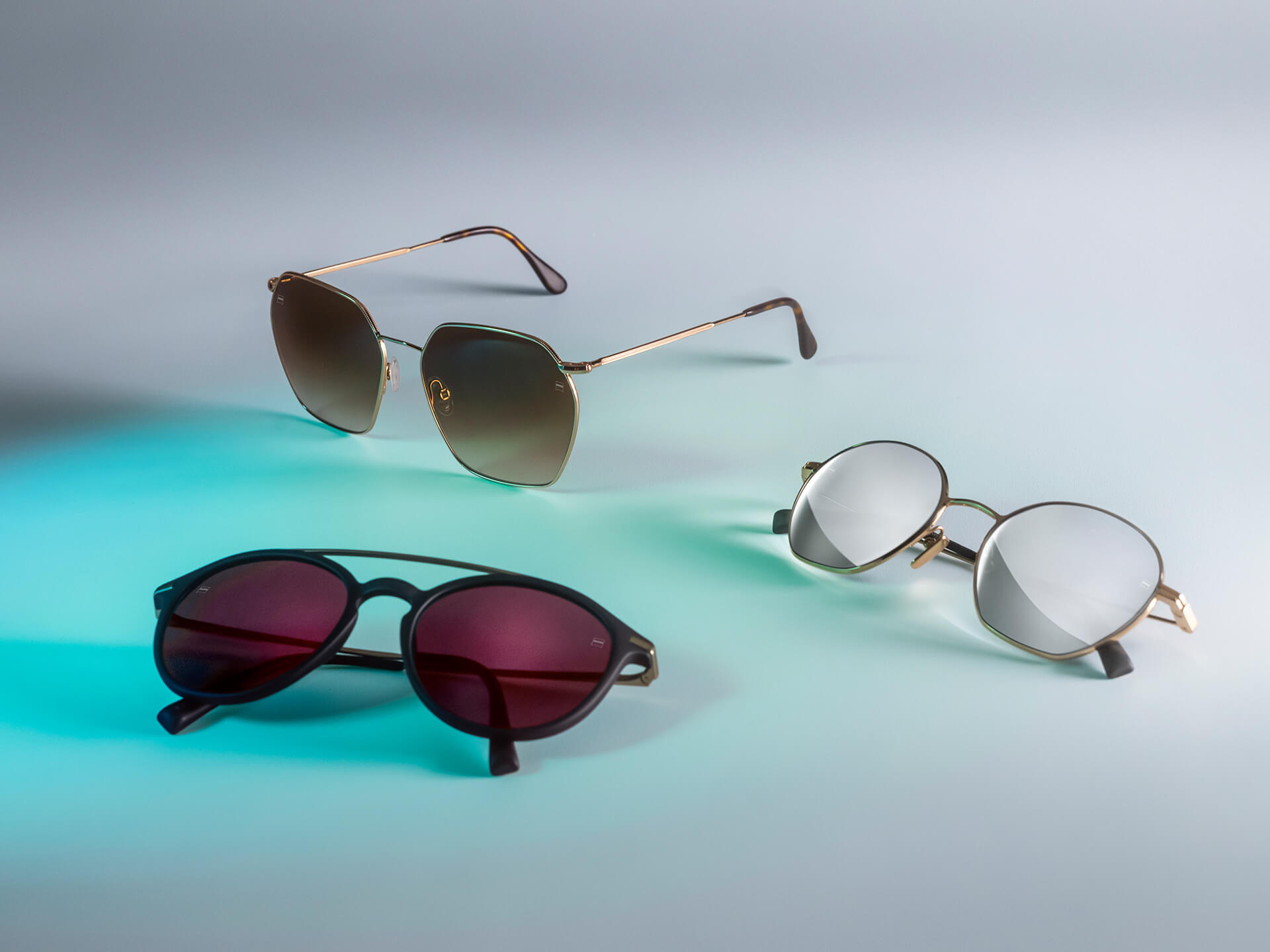 Drie zonnebrillen met verschillend gekleurde ZEISS brillenglazen, voorzien van DuraVision Sun, DuraVision Mirror en Flash Mirror coatings, zichtbaar op een witte achtergrond met blauwe lichtreflectie.