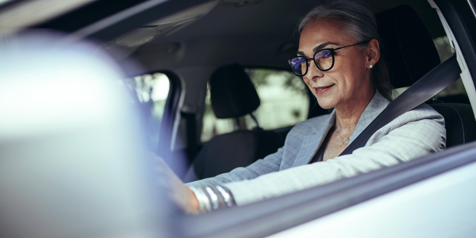 Een iets oudere vrouw in een auto draagt een bril met ZEISS DriveSafe brillenglazen.