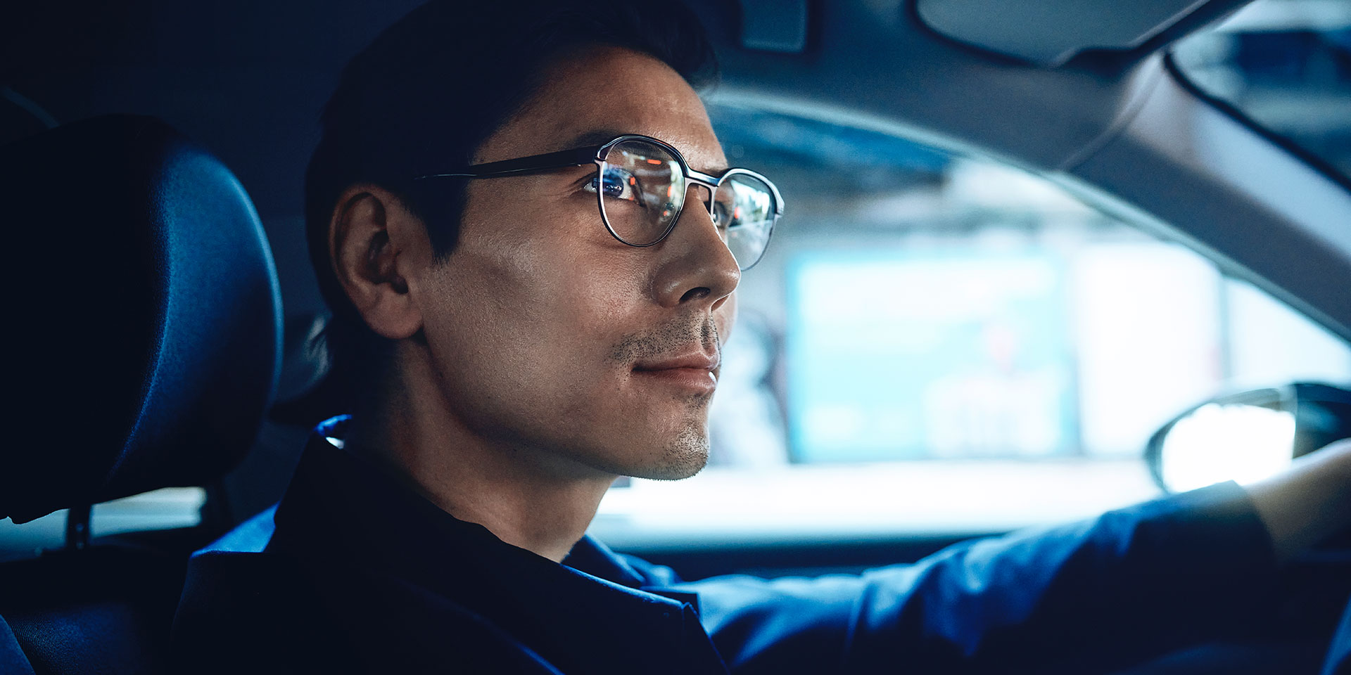 Een man die een auto bestuurt, ziet er zelfverzekerd uit met een kleine glimlach. Hij draagt ZEISS enkelvoudige DriveSafe brillenglazen
