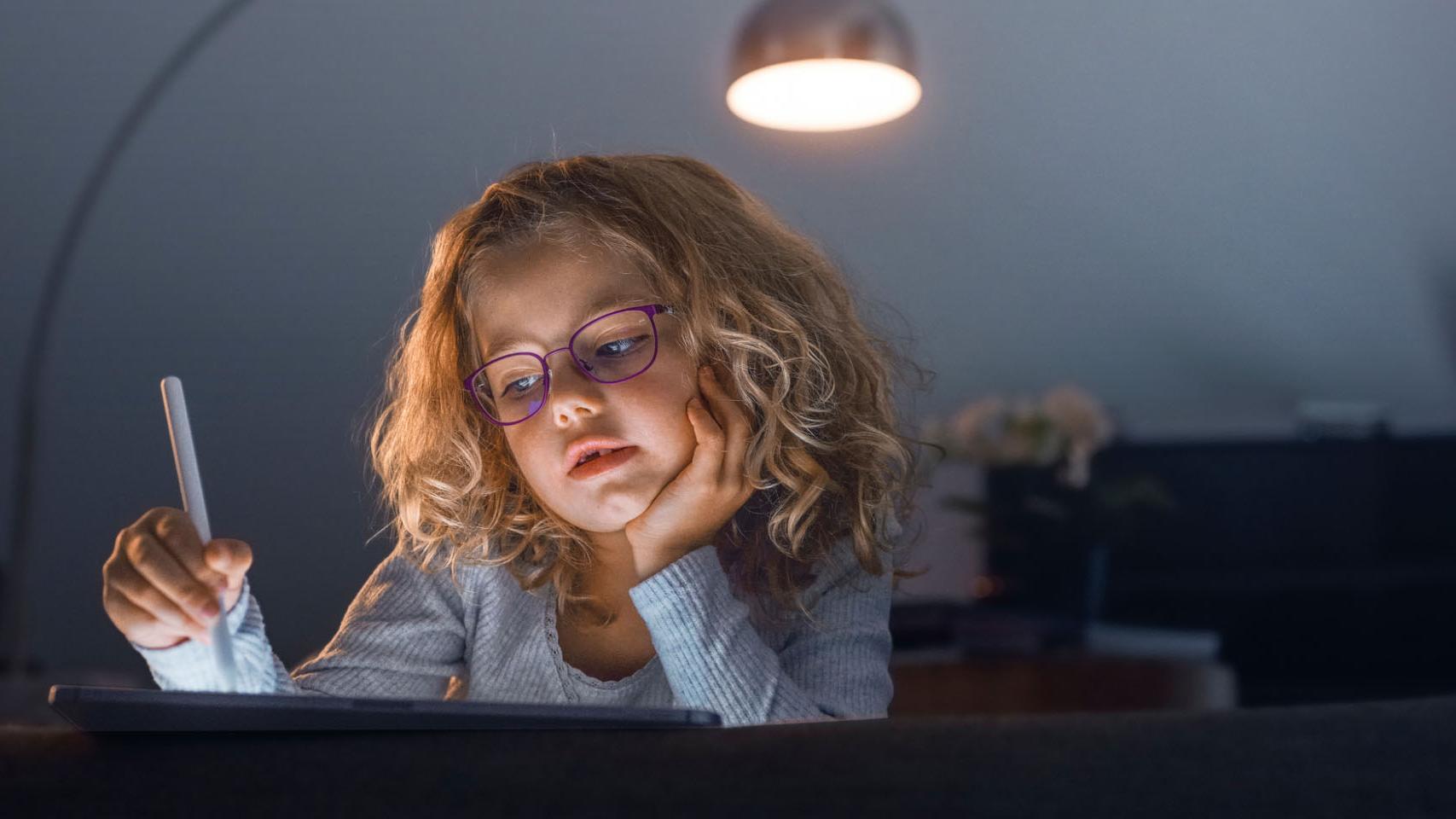 Een klein meisje in een donkere woonkamer kijkt naar een tablet.