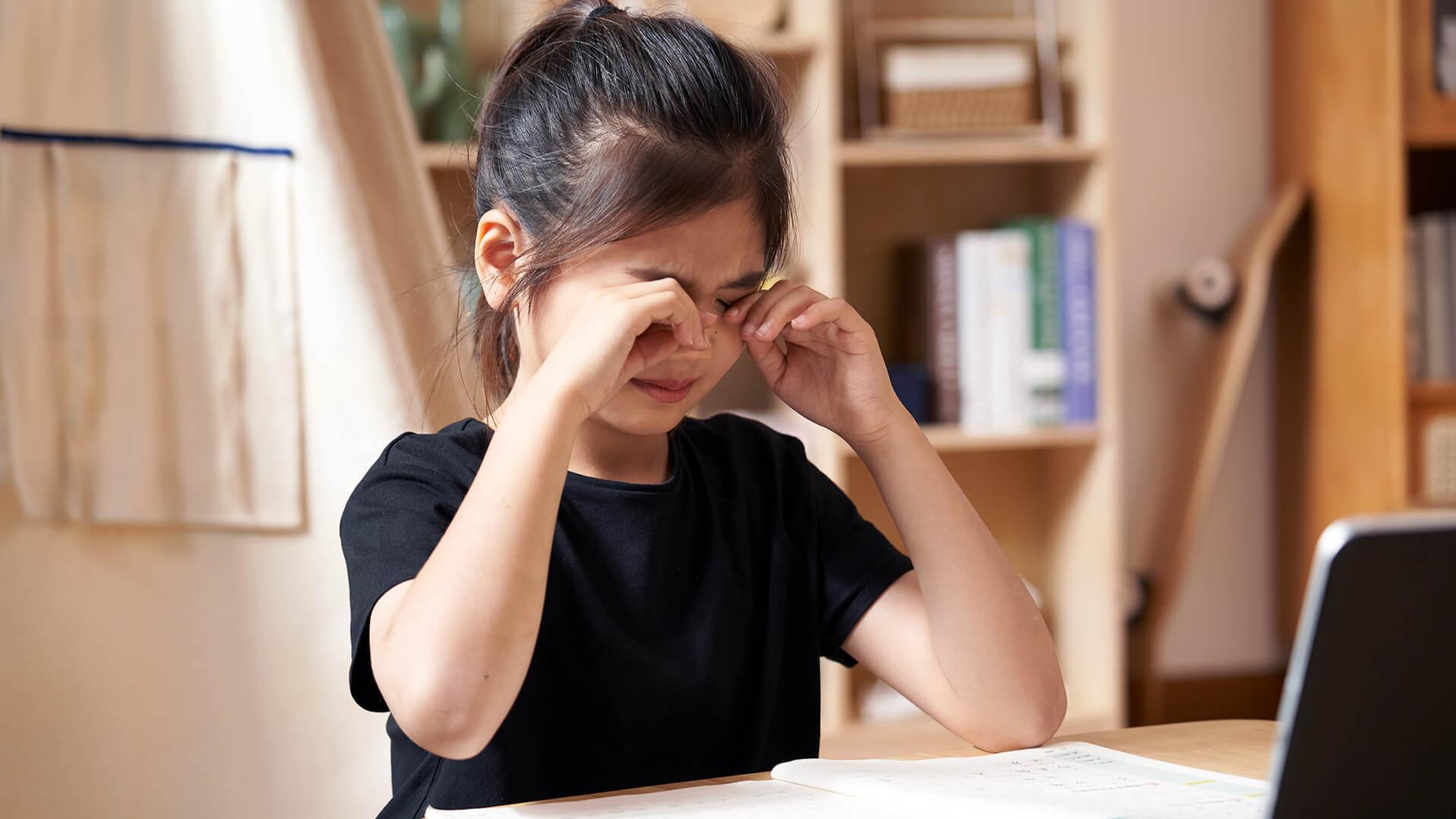 Une petite fille se frotte les yeux en faisant ses devoirs.