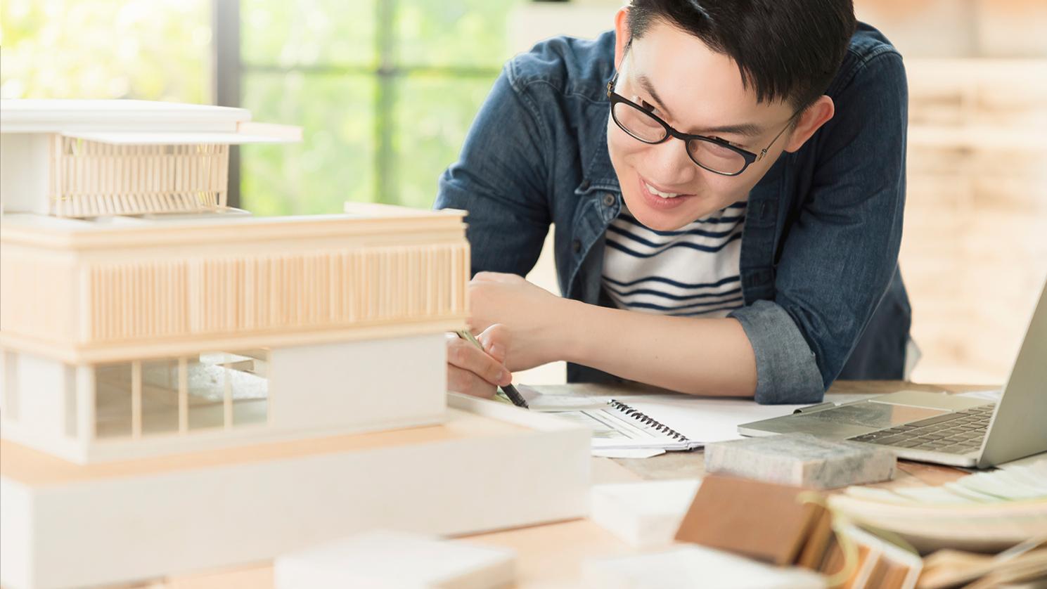 Man van middelbare leeftijd met kort zwart haar draagt een ZEISS Office bril om hem te helpen focussen op de details van een ingewikkeld architectuurmodel. 