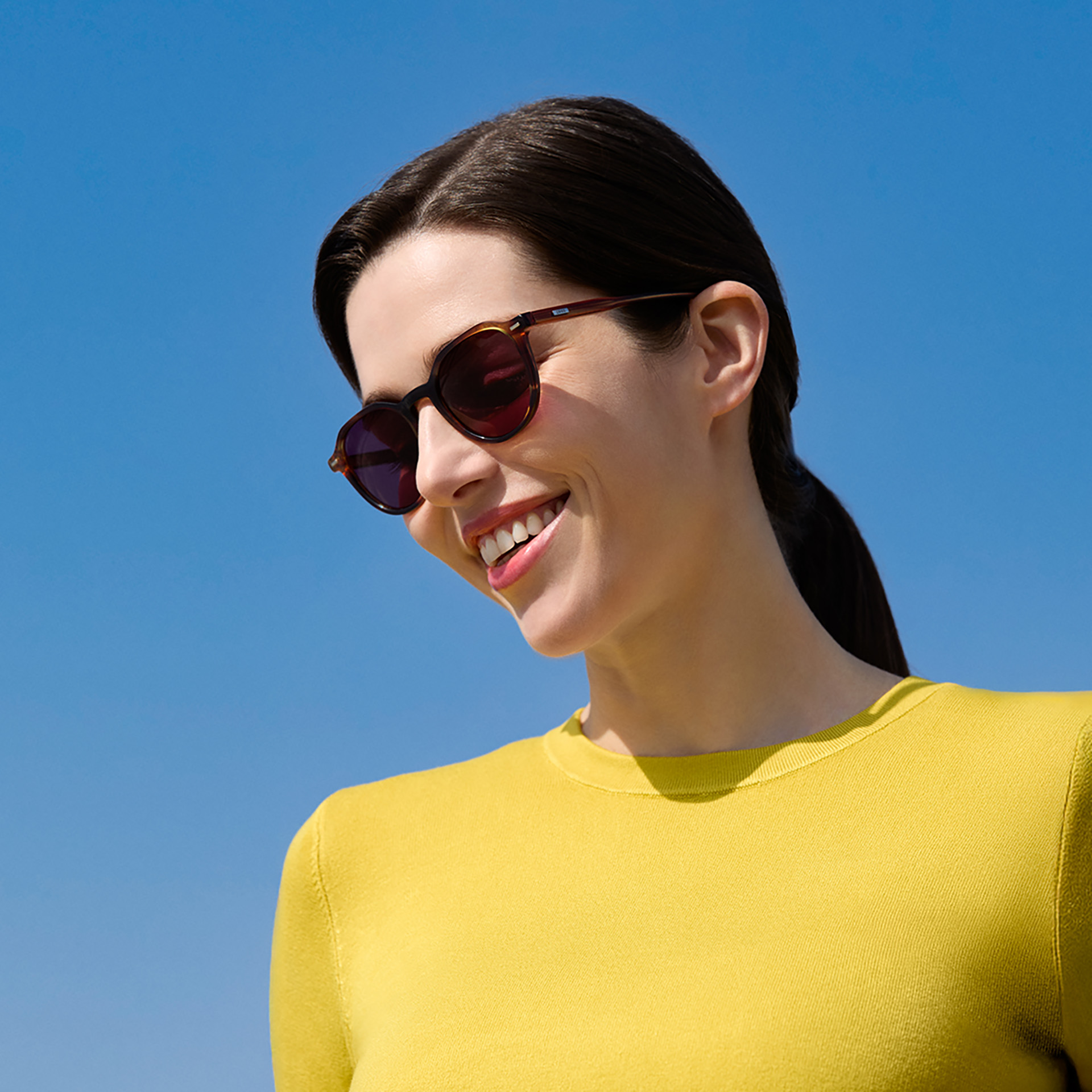 Une femme porte des lunettes de soleil correctrices ZEISS avec des verres en teinte bordeaux. 