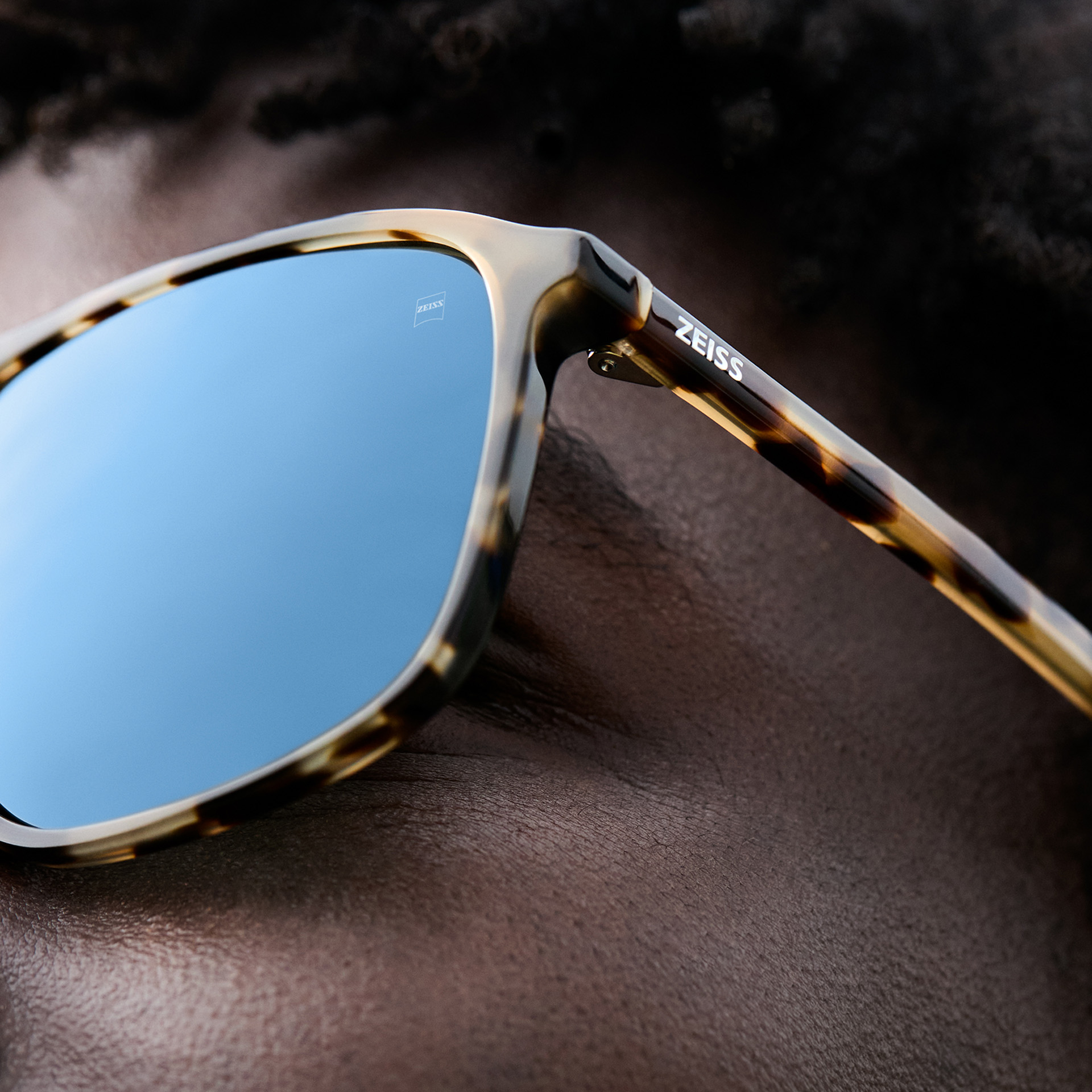 Plan rapproché d’un homme portant des lunettes de soleil écaille avec des verres qui reflètent le ciel bleu.