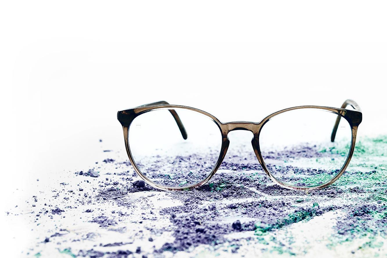 Een bril met heldere brillenglazen ligt op gekleurd poeder.