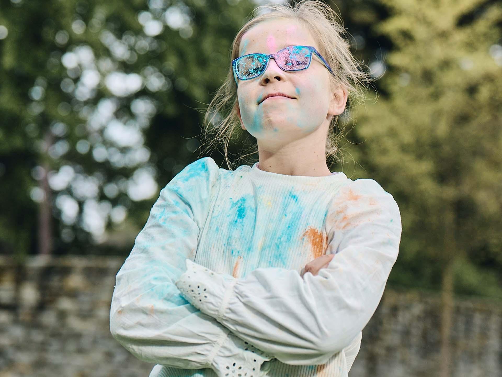 Une fillette, bras croisés, ses lunettes salies d’avoir joué avec de la poudre colorée, regarde l’objectif avec un sourire effronté.