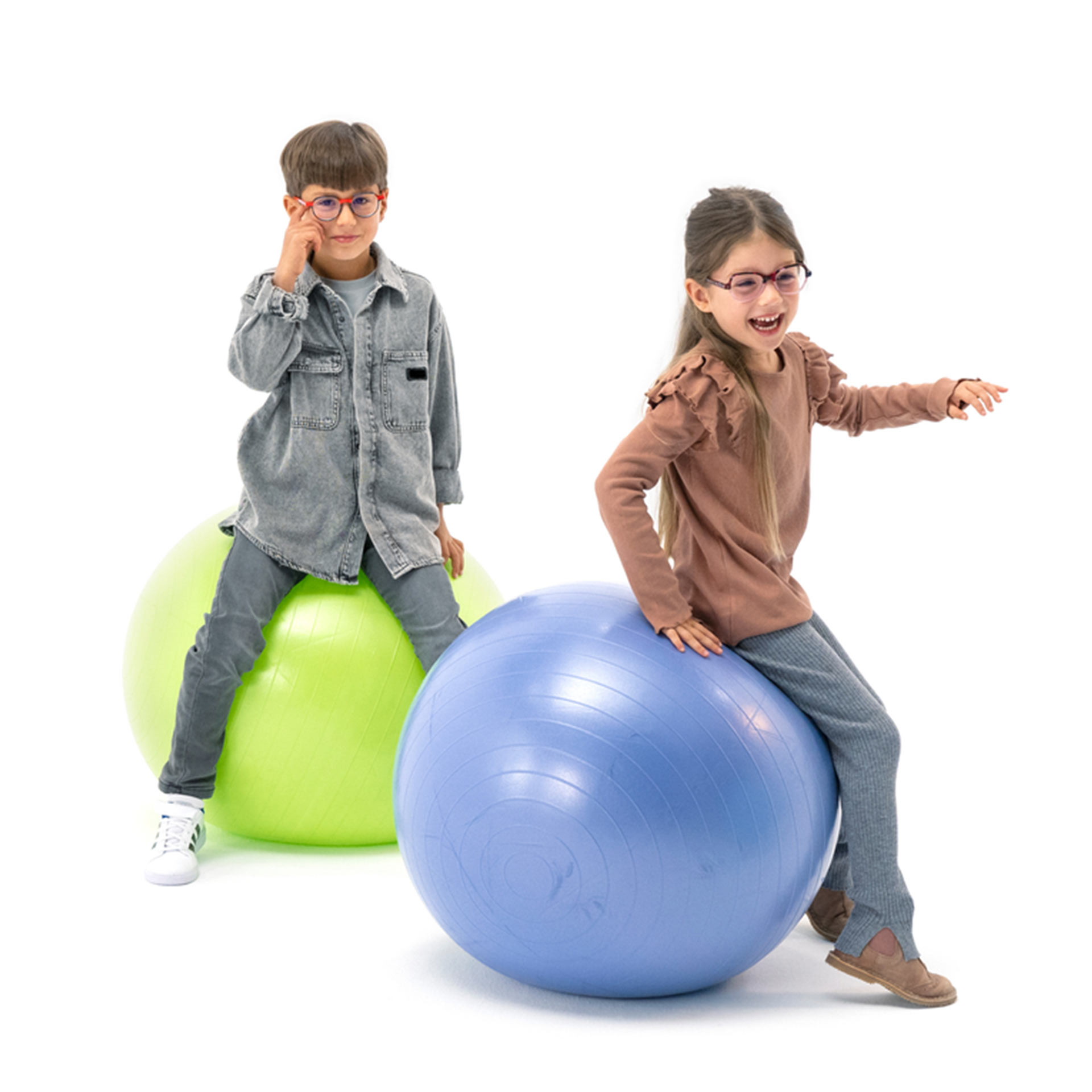 Un garçon et une fille, tous deux portant des lunettes, s’amusent sur des ballons de gymnastique.