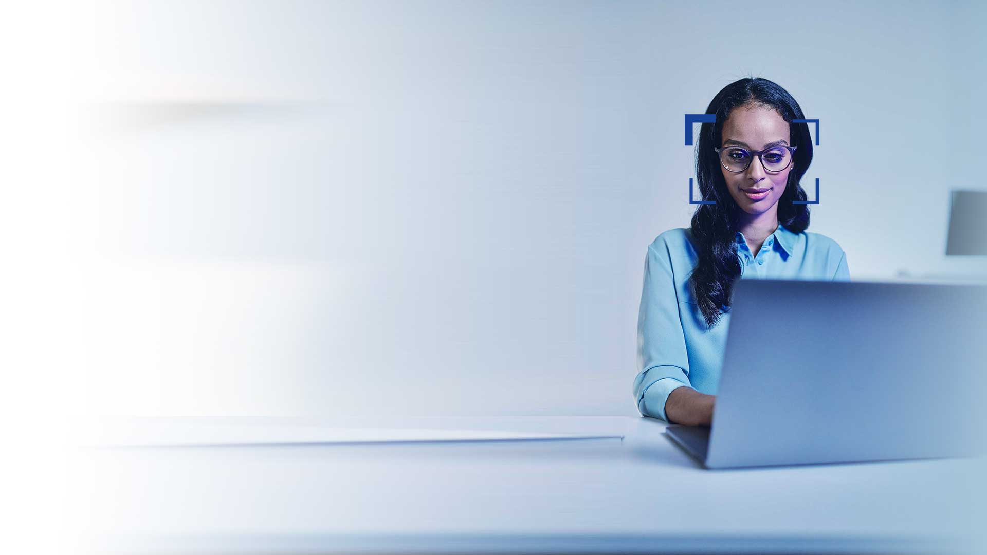 Vrouw met zwart haar en een bril kijkt met een lach op haar gezicht naar een laptop